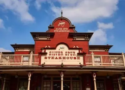 Restaurante elegante del Lejano Oeste en Disneyland París, con especialidad en carnes a la parrilla en horno de leña, servicio de mesa y un ambiente exclusivo inspirado en los salones del siglo XIX.
