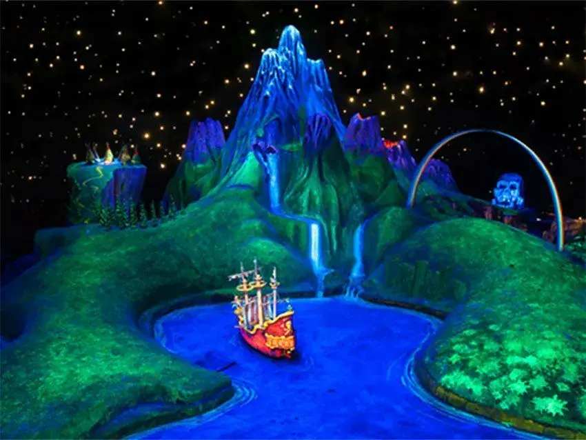Imagen nocturna de un barco iluminado en un lago con una montaña gigante al fondo en Peter Pan's Flight