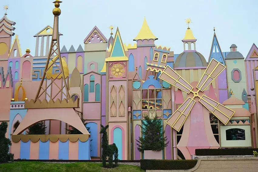 Vista de la fachada de la atracción It's a Small World, con árboles, temática Disney y molinete