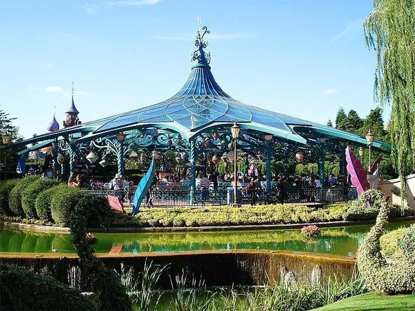 Vista panorámica exterior de la atracción Tazas Locas en Disneyland Paris, con visitantes esperando para subirse.
